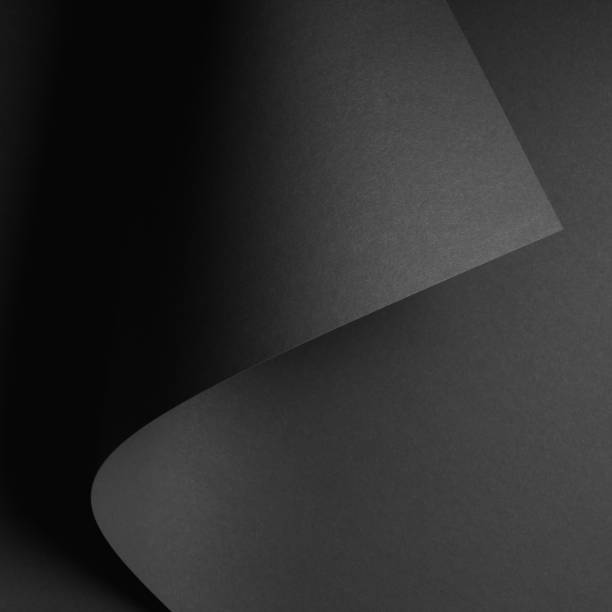 istock dark abstract background with black rolled paper sheet 976665558