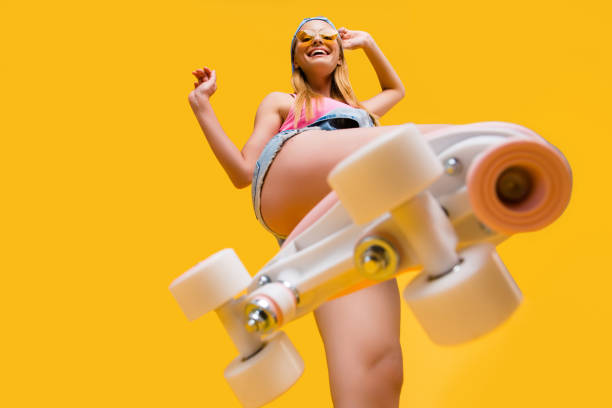 bottom view of roller skate step on camera, cheerful joyful playful funky girl showing equipment for fitness workout isolated on yellow background - shoe women retro revival fashion imagens e fotografias de stock