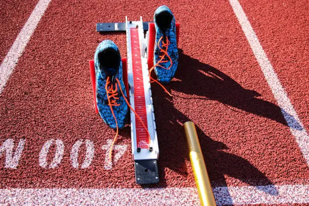 Starting blocks are set on at the 400 meter starting line wigh spikes and a baton on a red track.
