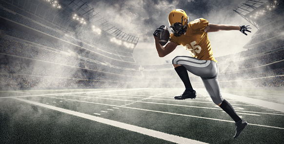 American football player jumps and catches the ball in flight in professional sport stadium with smoke and fog. Sportsman dressed in yellow sport uniform