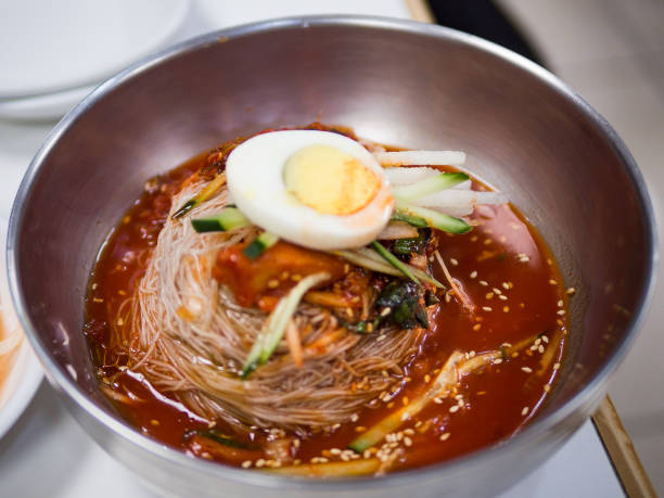 Close-up of Asian woman having Korean spicy noodle soup served in a traditional Korean metal pot