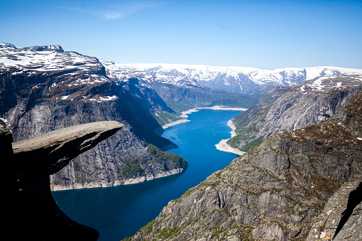 Amazing rock formation, making stone peak standing on top looking at Hardangerfjord. View is stunning as you can look how water from Atlantic Ocean squeezes trough narrow gaps between Norwegian mountains. In the distance you can see snowcapped mountain ranges.