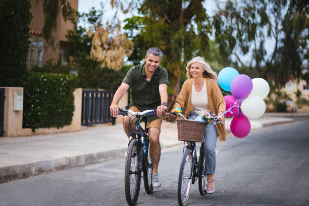 marito e moglie maturi che si godono il giro in bicicletta in periferia - mature adult bicycle senior adult heterosexual couple foto e immagini stock