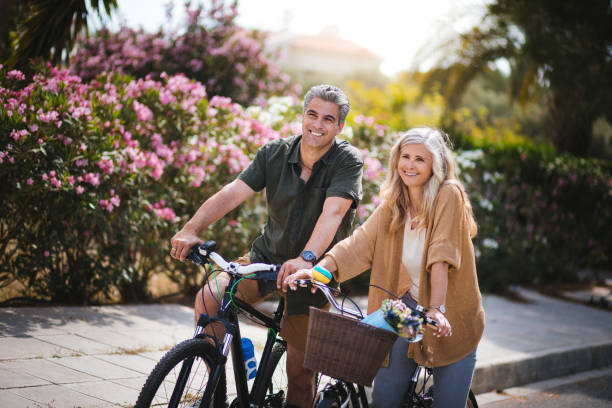 smiling active senior man and woman riding bicycles in spring - spring happiness women latin american and hispanic ethnicity imagens e fotografias de stock
