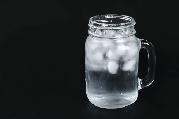 Ice water with ice and a mint leaf and a straw in a mason jar on a black background