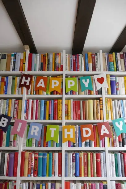 Photo of Happy birthday letters hanging on bookshelf in library