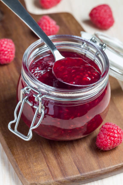 istock Raspberry jam in glass jar on a wooden board, vertical 976789634