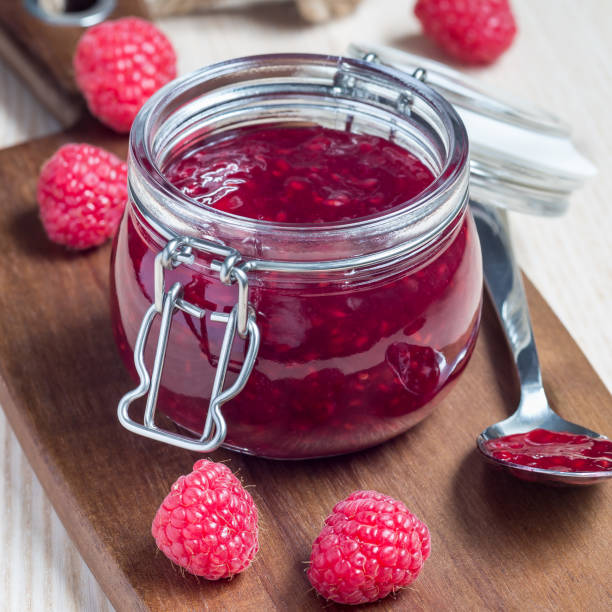 istock Raspberry jam in glass jar on a wooden board, square format 976789646