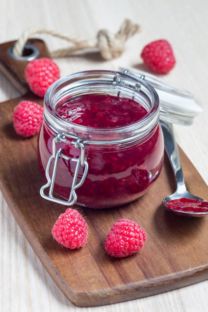 istock Raspberry jam in glass jar on wooden board, vertical 976789862