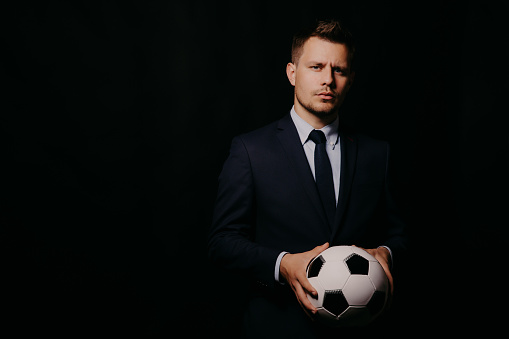 young handsome businessman holding a football on black background studio. blue jacket and tie. Stylish hairstyle model. World Championship.