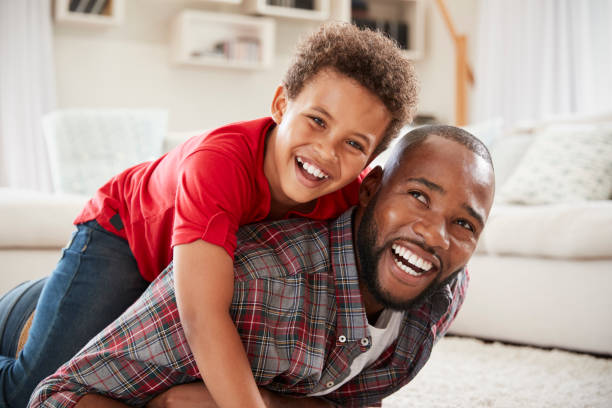istock Son Climbs On Fathers Back As They Play Game In Lounge Together 976807722