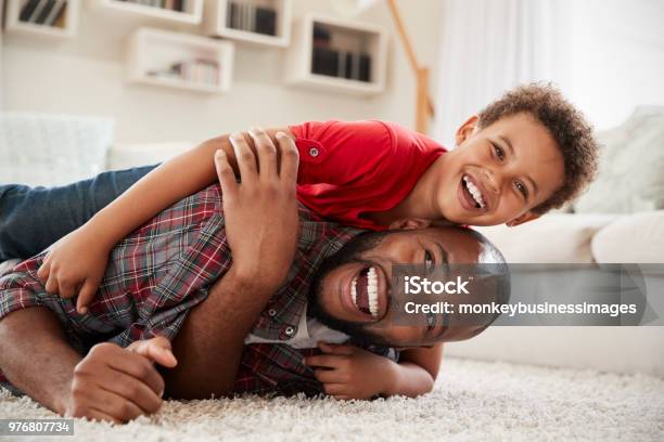 Son Climbs On Fathers Back As They Play Game In Lounge Together Stock Photo - Download Image Now