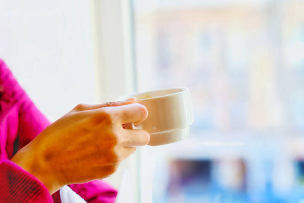 Hand of a women with a cup of coffee in white color in the morning time. stock photo