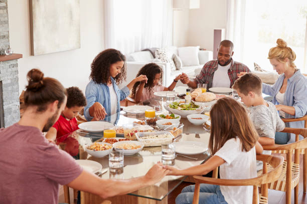 две семьи молятся перед тем, как наслаждаться едой дома вместе - saying grace стоковые фото и изображения