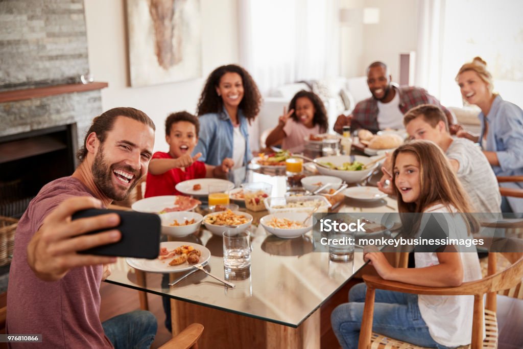 Due famiglie che si fanno selfie mentre si godono il pasto a casa insieme - Foto stock royalty-free di Famiglia