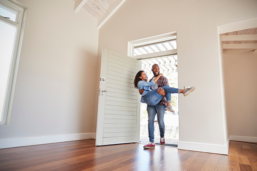 Man Carrying Woman Over Threshold Of Doorway In New Home