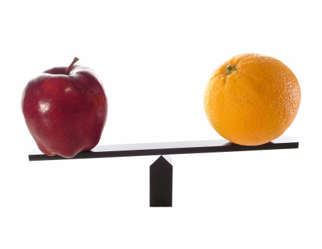 Metaphor of comparing apples to oranges on a balance beam isolated on white and the oranges are not as heavy or light.