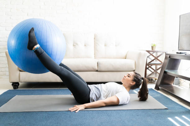 Fit woman lifting exercise ball with legs Side view of fit young woman lifting swiss ball with her feet. Legs workout with swiss ball. fitness ball photos stock pictures, royalty-free photos & images