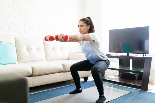 Squats routine at home Fit latin woman doing squats workout with weights in hand exercise room photos stock pictures, royalty-free photos & images