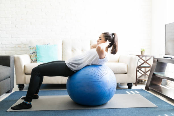 Woman on swiss ball doing abs exercise Side view of fit young latin woman doing abs exercise on swiss ball in living room fitness ball photos stock pictures, royalty-free photos & images