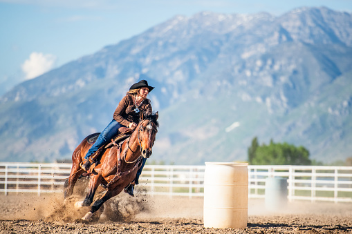 A woman concentrates as she rides her horse around a barrel at speed during a timed barrel racing event.