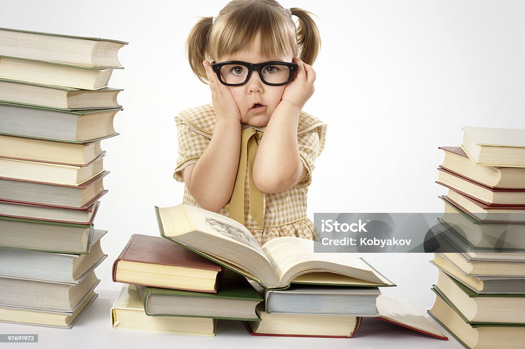 Worried little girl wearing glasses, surrounded by books Worried little girl wearing glasses, surrounded by books, back to school, isolated over white Activity Stock Photo