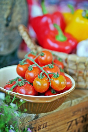 Fresh, raw vegetables for cooking:red and juicy vine-ripened cherry tomatoes in a ramekin with colorful bell peppers background. Selective focus.