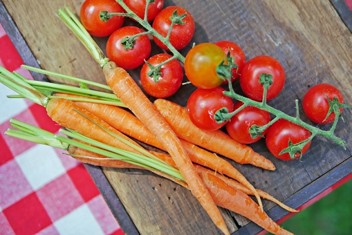 Fresh, raw vegetables for cooking:carrots and red vine-ripened cherry tomatoes on a wooden cutting board. Top view.