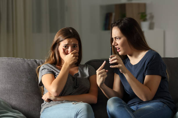 Girl scolding her sad friend about media content Girl scolding her sad friend about media content sitting on a couch in the living room at home sheepish look stock pictures, royalty-free photos & images