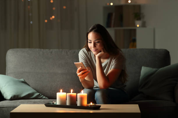 Relaxed girl using phone in the night with candle lights Relaxed girl using phone in the night with candle lights sitting on a couch in the living room at home blackout photos stock pictures, royalty-free photos & images