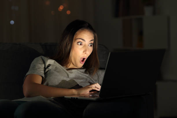 暗闇の中でオンライン コンテンツを見て驚かれる女性 - dark humor ストックフォトと画像