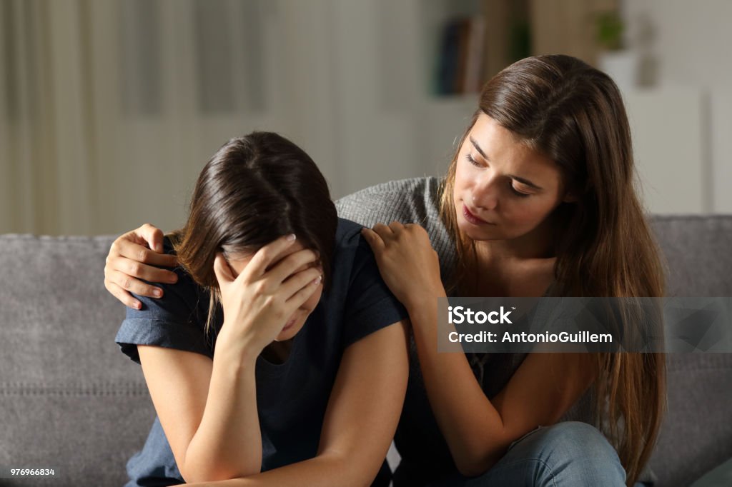 Teen comforting hes sad friend in the night Teen comforting hes sad friend in the night sitting on a couch in the living room at home Friendship Stock Photo