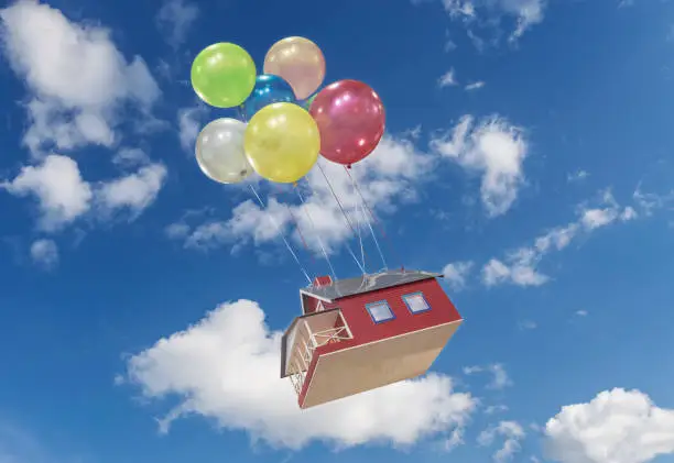A small, toy house flies across the sky on colorful balloons