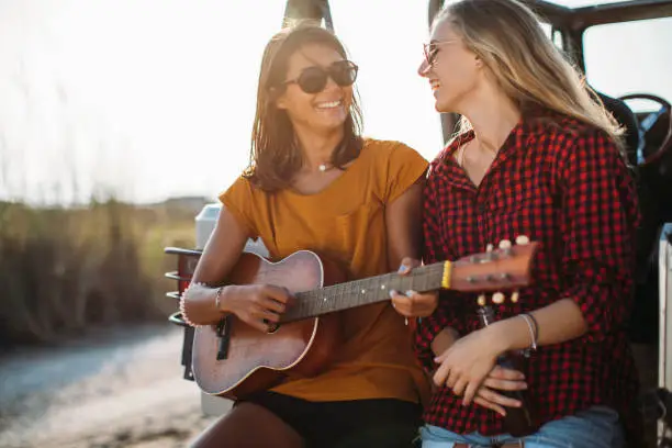 Two girlfriends enjoying time together on a roadtrip playing a guitar