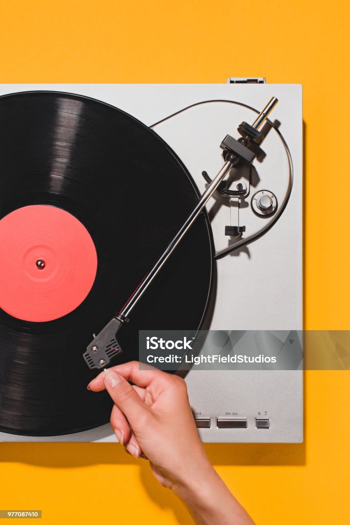 cropped shot of woman turning on vinyl player isolated on yellow Record - Analog Audio Stock Photo