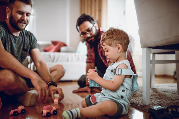 coppia gay che gioca con il figlio adottivo e i suoi giocattoli - people joy relaxation concentration foto e immagini stock