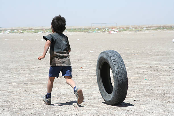 Young impoverished boy playing with a car tire on dirt patch A little boy playing with tire near his home at a garbage dump. poverty mexico environment slum stock pictures, royalty-free photos & images