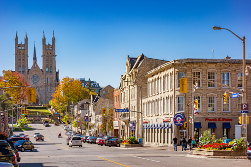 People walk along Macdonell street in downtown Guelph Ontario Canada on a sunny day, with the Basilica of our Lady Immaculate in the background.
