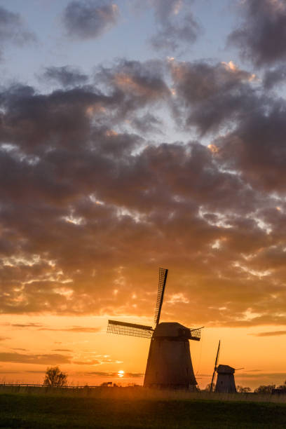 istock Two windmills in silhouette with the sun setting in Netherlands 977122924