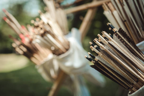 Female archer preparing her bow for target practice, focusing intently on her aim at an outdoor archery range surrounded by trees
