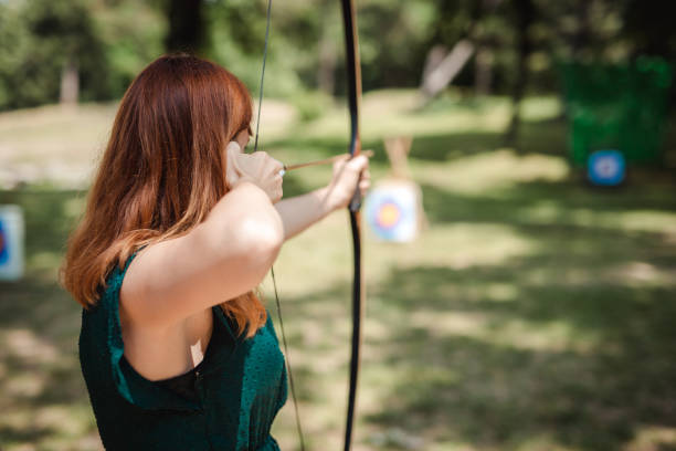 Young redhead woman practicing archery in the field