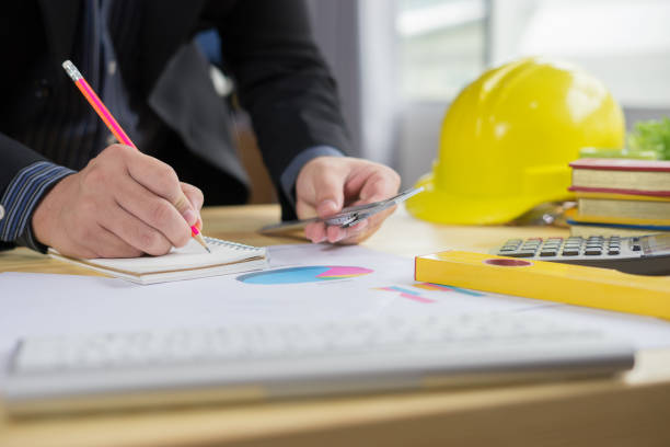 istock Architects working on blueprint with pencil,engineer inspective in workplace ,architectural project, blue prints,ruler,calculator,laptop and yellow helmet. Construction concept. Engineering tools 977159904