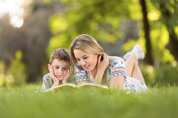 istock Young mother and son lying ona grass in park and reading a book 977221046