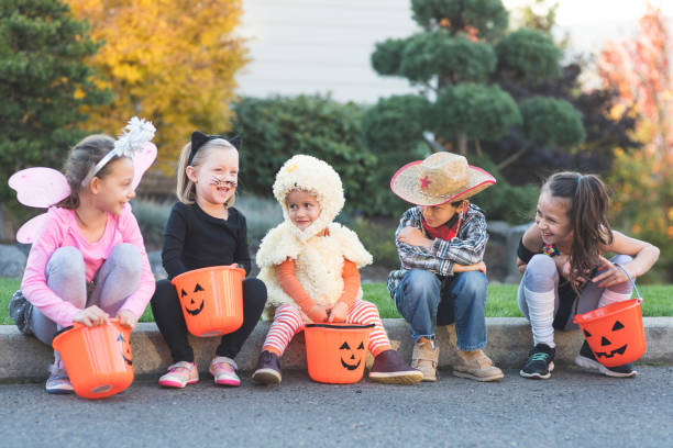 Multiethnic group of kids trick or treating A multiethnic group of kids go trick or treating in a residential neighborhood. They're all sitting on a curb hanging out with their pumpkin candy buckets. There's a fairy, a black cat, a duck, a cowboy, and an exercise instructor. trick or treat photos stock pictures, royalty-free photos & images