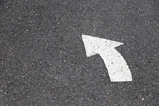 White painting in turn left direction arrow symbol on black asphalt road background