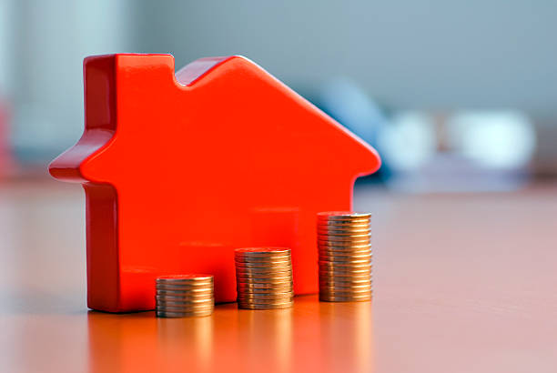 Red 3D house model next to growing stacks of coins stock photo