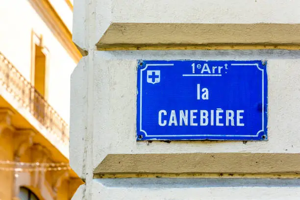 Photo of Close-up view of the street name sign of La Canebiere, the historic high street and most famous avenue in Marseille, France, mounted on the corner of a building, with an old building in the background