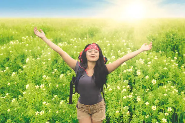 Female hiker carrying backpack while enjoying fresh air in the flower field