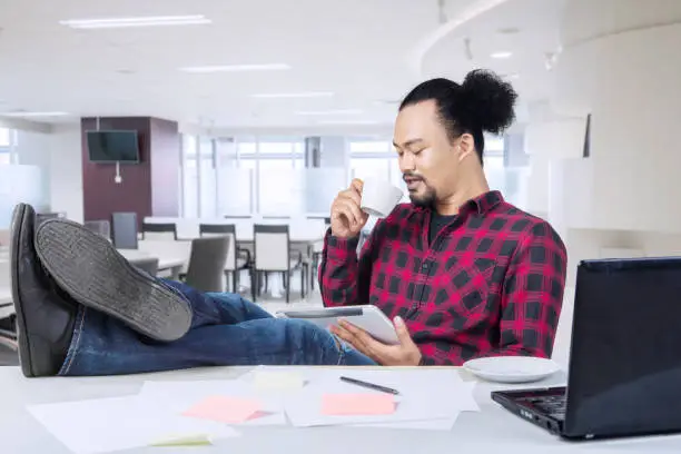Happy professional worker drinking a cup of coffee and feet on desk in a modern office