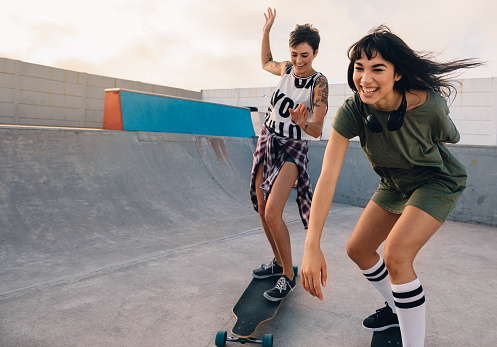 Young hipster girls riding on skateboards and having fun. Female friends together skateboarding at skate park.